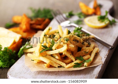 French fries on tracing paper on board on wooden table - stock photo