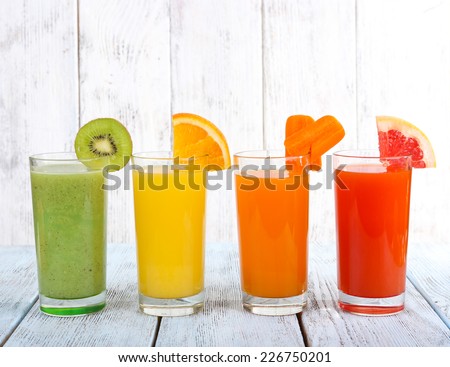 Fruit and vegetable juice in glasses and pieces of fresh fruits on wooden table on wooden wall background