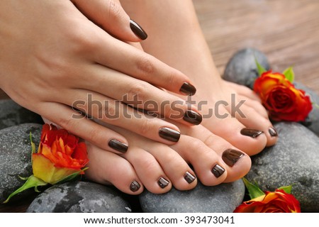 Manicured female feet and hand with flowers on spa stones closeup