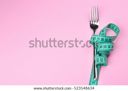 Measuring tape wrapped around fork lying on color surface. Diet concept
