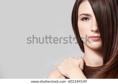 Beautiful young woman with long straight hair on light background