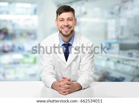 Male pharmacist near counter at work. Blurred shelves with pharmaceutical products on background