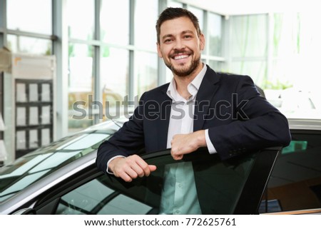 Handsome car salesman standing near automobile in dealership centre