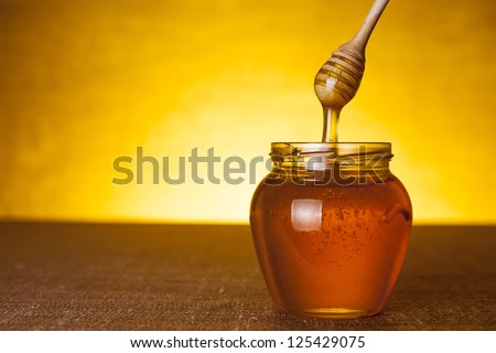 Honey jar with dipper and flowing honey, canvas background