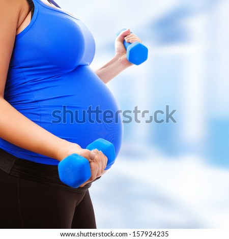 Pregnant female do exercise in sports hall, side view, body part, lifting dumbbells, active and sportive pregnancy, healthy motherhood concept