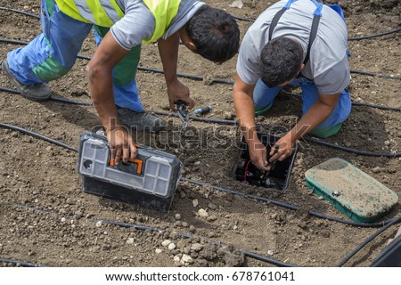Garden workers installing irrigation control box for water plants with automatic watering system.