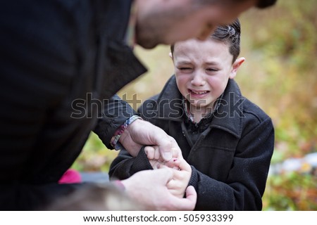 A Small boy crying in pain injuring his hand. Father provides first aid