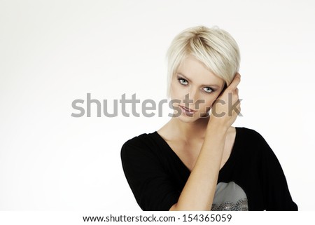 Beautiful young woman staring at the camera with a serious expression and her hand raised to her short trendy blond hair holding her fringe clear of her face, isolated on white with copyspace