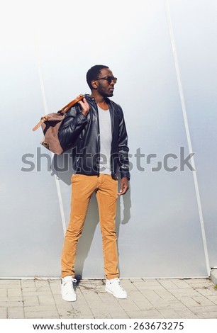 Outdoor fashion portrait of handsome african man in black rock leather jacket with bag standing against the shiny metal wall