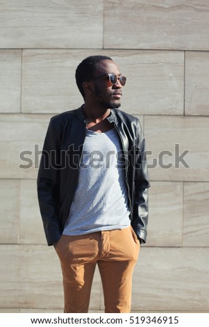 Fashion african man wearing a sunglasses and black rock leather jacket over textured background evening in city