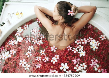Woman relaxing in round outdoor bath with tropical flowers, organic skin care, luxury spa hotel, lifestyle photo, top view