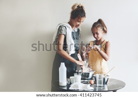 Mom with her 10 years old daughter dressed in linen aprons are cooking together over light wall, lifestyle photo series
