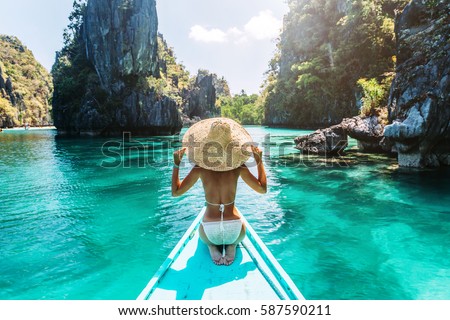 Back view of the young woman in straw hat relaxing on the boat and looking forward into lagoon. Travelling tour in Asia: El Nido, Palawan, Philippines.
