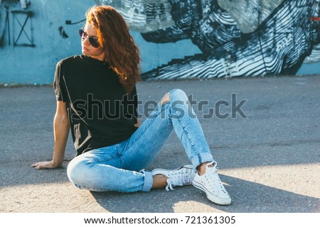 Model wearing plain black t-shirt, boyfriend jeans, sneakers and hipster sunglasses posing against street wall, teen urban clothing style, mockup for tshirt print store