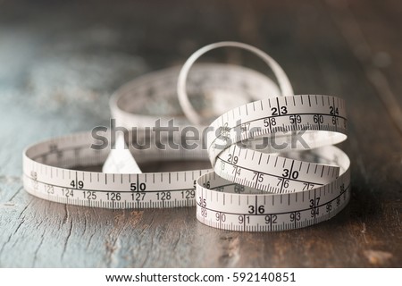 Close up tailor measuring tape on wooden table background. White measuring tape shallow dept of field.