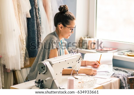 Close up. hands woman Tailor working cutting a roll of fabric on which she has marked out the pattern of the garment she is making with tailors chalk.