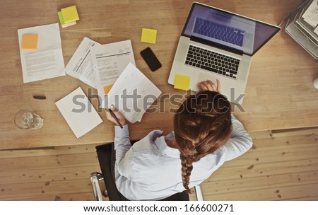 High angle view of an young brunette working at her office desk with documents and laptop. Businesswoman working on paperwork.