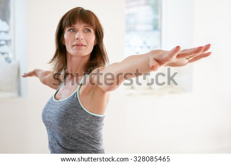 Portrait of mature woman stretching her arms and looking away at gym. Beautiful woman performing yoga in warrior pose, Virabhadrasana.