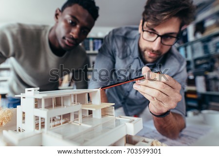 Two young architects working on new architectural house model. Designers looking at house model in studio.