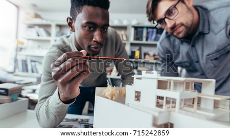Two male architects in office discussing construction project. Young men working together on new building model.