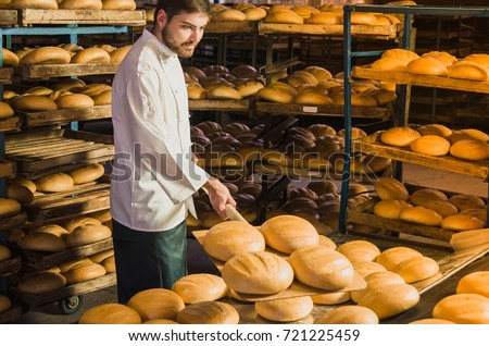 Baker. A young handsome bakery worker on the background of bread, takes bread from a stove with a wooden shovel. Industrial production of bakery products. a man in the baker's special clothing. Bakery
