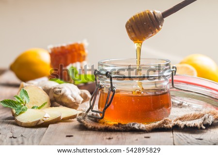 Honey in jar with honey dipper, ginger and lemon on wooden background