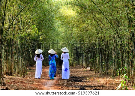 The charming slender girl in traditional ao dai Vietnam goes in bamboo forest.