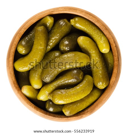 Cornichons, pickled cucumbers in wooden bowl. Green tart French pickles, made from small gherkins. Gherkin, commonly known as pickle. Isolated macro food photo close up from above on white background.