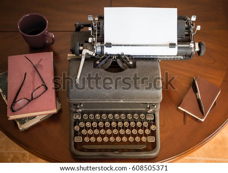 black vintage typewriter sitting on brown wooden table next to brown leather notepad and pen, and old books and stylish glasses. any author, writer, editor or journalist can type a creative story