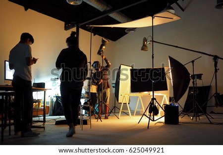 Silhouette of people working in production studio for shooting or recording by digital camera and lighting set.