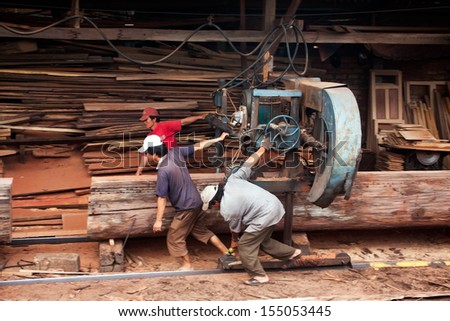 QUY NHON, VIET NAM, JUNE 18: Three woodworker try to pull cumbersome machine to split section of a tree trunk into plank at sawmill. June 18, 2012