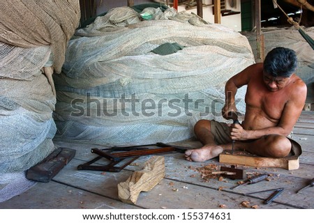 CA MAU. VIET NAM- JUNE 29. The man with carpentry tool bore a hole in section of a tree trunk, at him back, there are some fishing net roll to fisherman catch fish. June 29, 2013