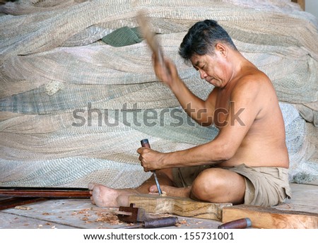 CA MAU, VIET NAM- JUNE 29. Portrait of the man with carpentry tool bore a hole in section of a tree trunk, at him back, there are some fishing net roll to fisherman catch fish. June 29, 2013