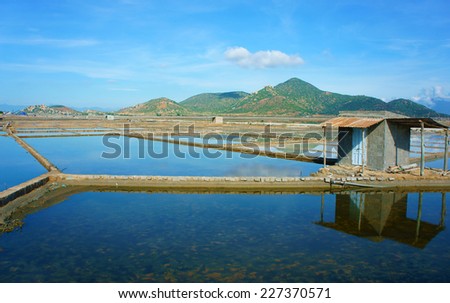 Beautiful landscape of salina filed on day under blue sky, store house reflect on saltwater, chain of mountain behind, amazing scene of agriculture at Vietnamese countryside