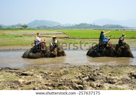 BUON ME THUOT, VIET NAM- FEB 25: Group of tourist traveling Vietnamese countryside, traveler ride elephant, cross rural with green flield, this is Daklak's travel product, Vietnam, Feb 25, 2015