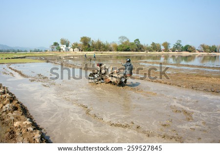 DAK LAK, VIET NAM- FEB 25: Asian farmer working on rice field, Vietnamese man plough paddy plantation for new crop by tractor, repair soil for sow rice in hot day, Daklak, Vietnam, Feb 25, 2015