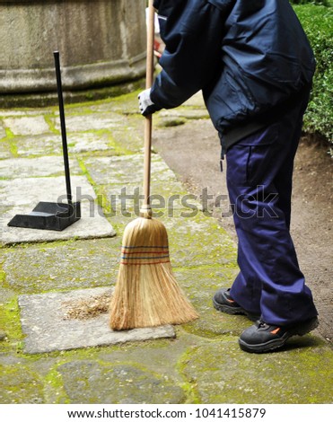 Sweeper, municipal cleaning worker sweeping autumn leaves in the garden
