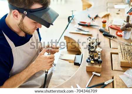 Portrait of jeweler making ring decoration in workshop, forming and polishing it on work station with different tools