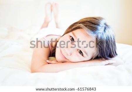 Happy, smiling child lying down, looking straight into the camera with focus on her face in sunlight