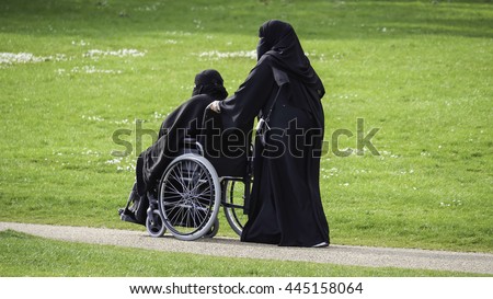 stock-photo-muslim-women-in-burkas-in-a-park-one-pushing-the-other-in-a-wheelchair-445158064.jpg