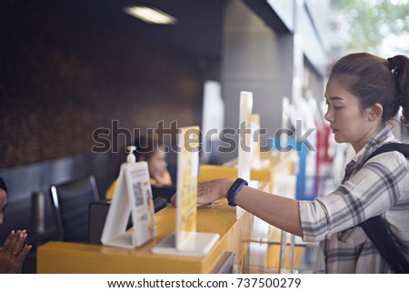 Airline staff giving Identity card and ticket back to young asian woman at airport check-in counter.