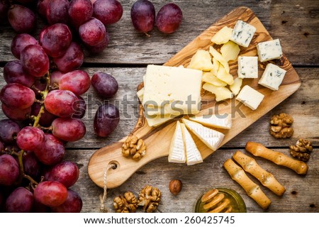 Cheese plate: Emmental, Camembert cheese, blue cheese, bread sticks, walnuts, hazelnuts, honey, grapes on wooden table