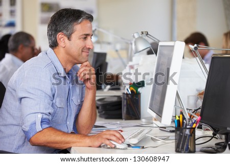 Man Working At Desk In Busy Creative Office Man Working At Desk In Busy Creative Office
