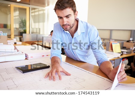 Male Architect With Digital Tablet Studying Plans In Office