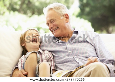 Grandfather With Grandson Reading Together On Sofa