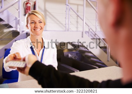 Staff At Airport Check In Desk Handing Ticket To Passenger