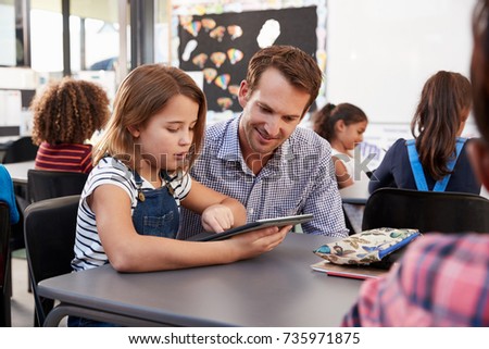 Teacher and young schoolgirl using tablet in classroom