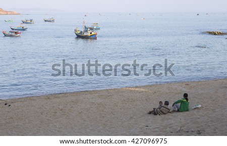 Quy Nhon, Vietnam - Apr 20, 2016: Fisherman family relax on the beach and watching fishing boat returning to the harbor at sunset in the end of the day.