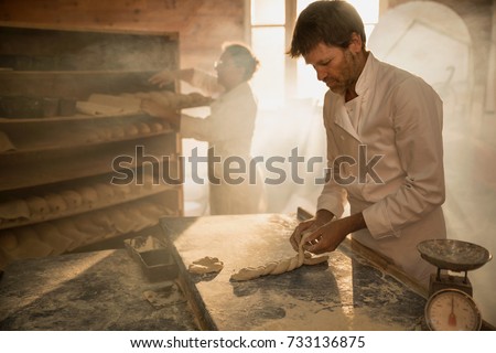 In a traditional bakery, bakers prepare the dough for the bread. The morning sun comes in through the window
