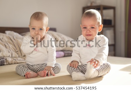 crying baby sitting on a bed with his twin